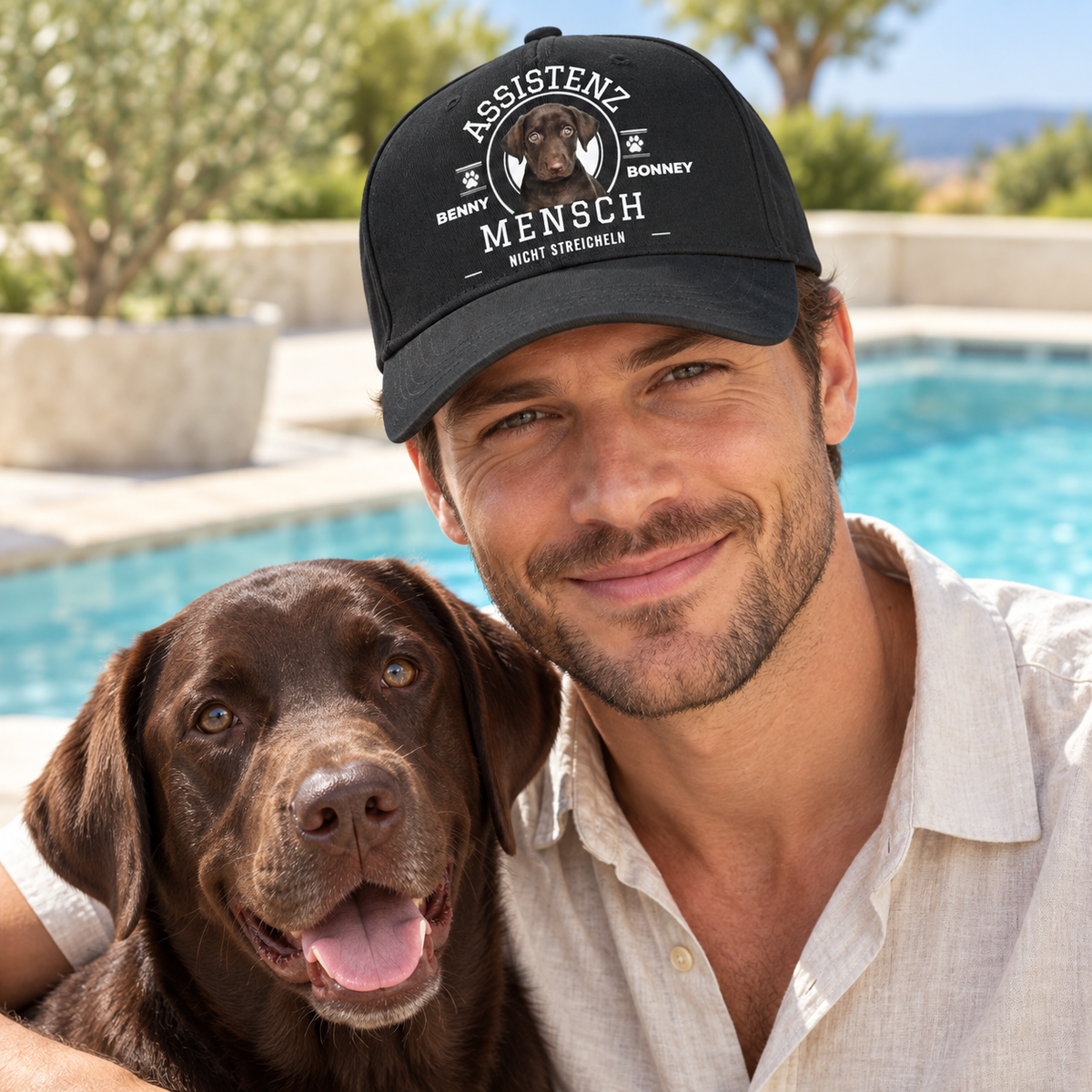 Cappellino nero con stampa “ASSISTENZ MENSCH”, accanto a un uomo sorridente e un cane marrone.