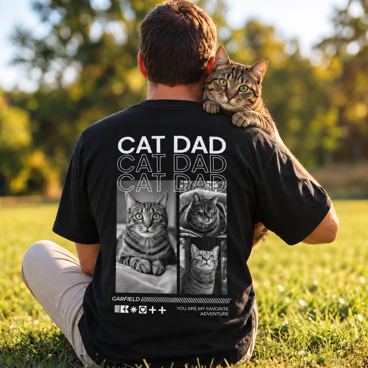 T-shirt nera con la scritta "Cat Dad" e motivi di gatti, indossata da una persona con un gatto.
