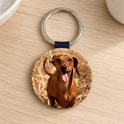 Portachiavi rotondo con foto di un cane sorridente su un tavolo in legno.