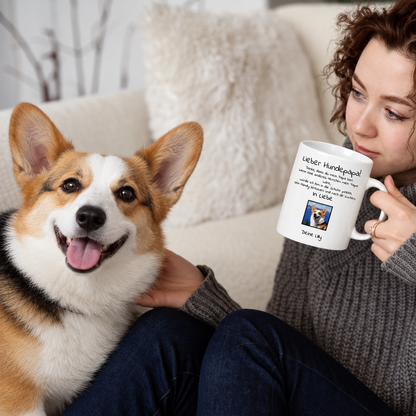 Persona che beve da una tazza bianca con la scritta "Lieber Hundepapa", un cane seduto accanto.