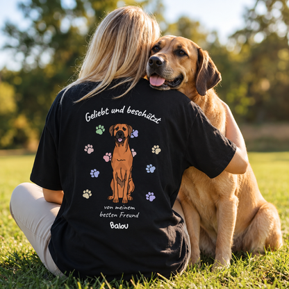 T-shirt nera con la scritta "Geliebt und beschützt", un cane e impronte colorate.