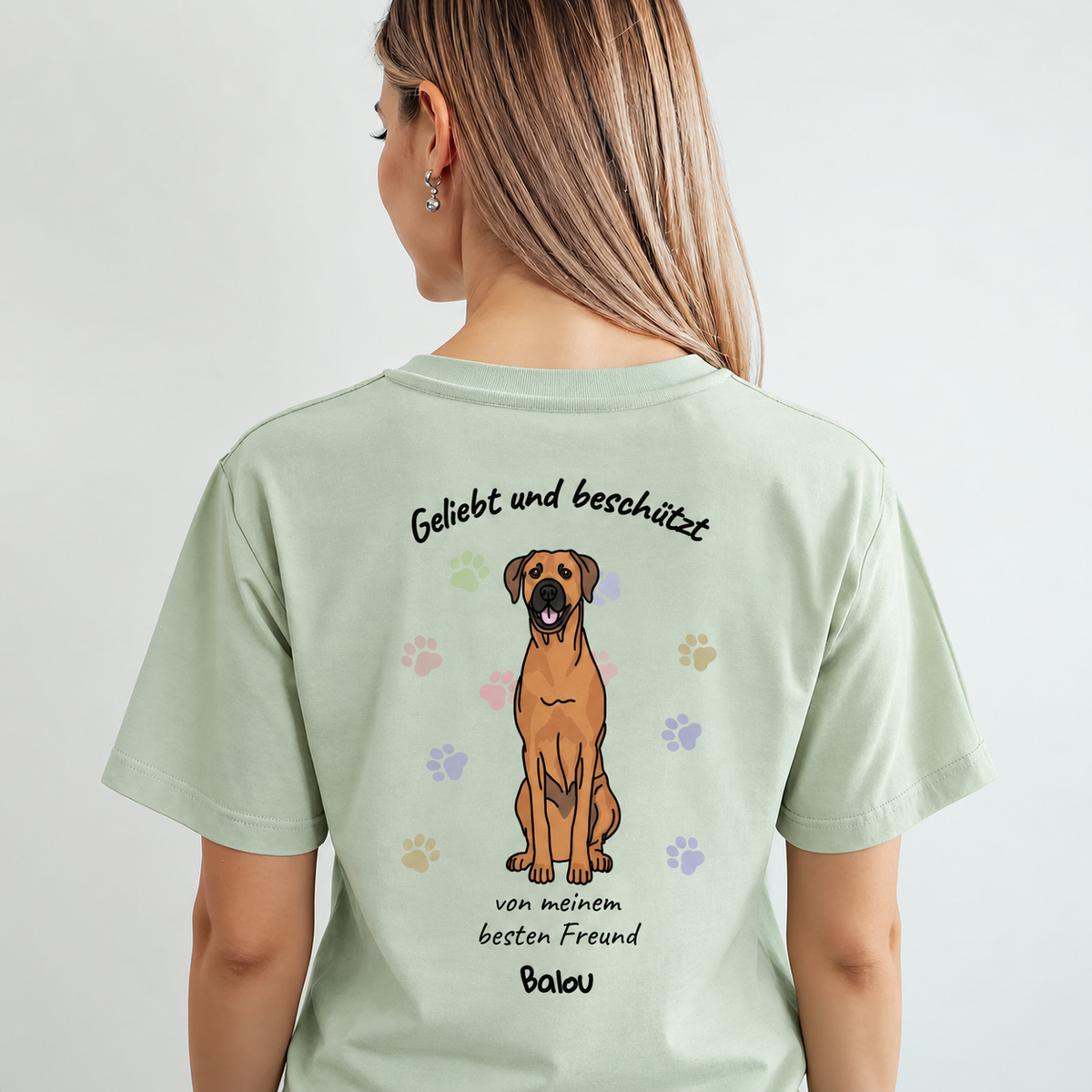 T-shirt verde chiaro con stampa di cane e il testo "Geliebt und beschützt" sul retro.