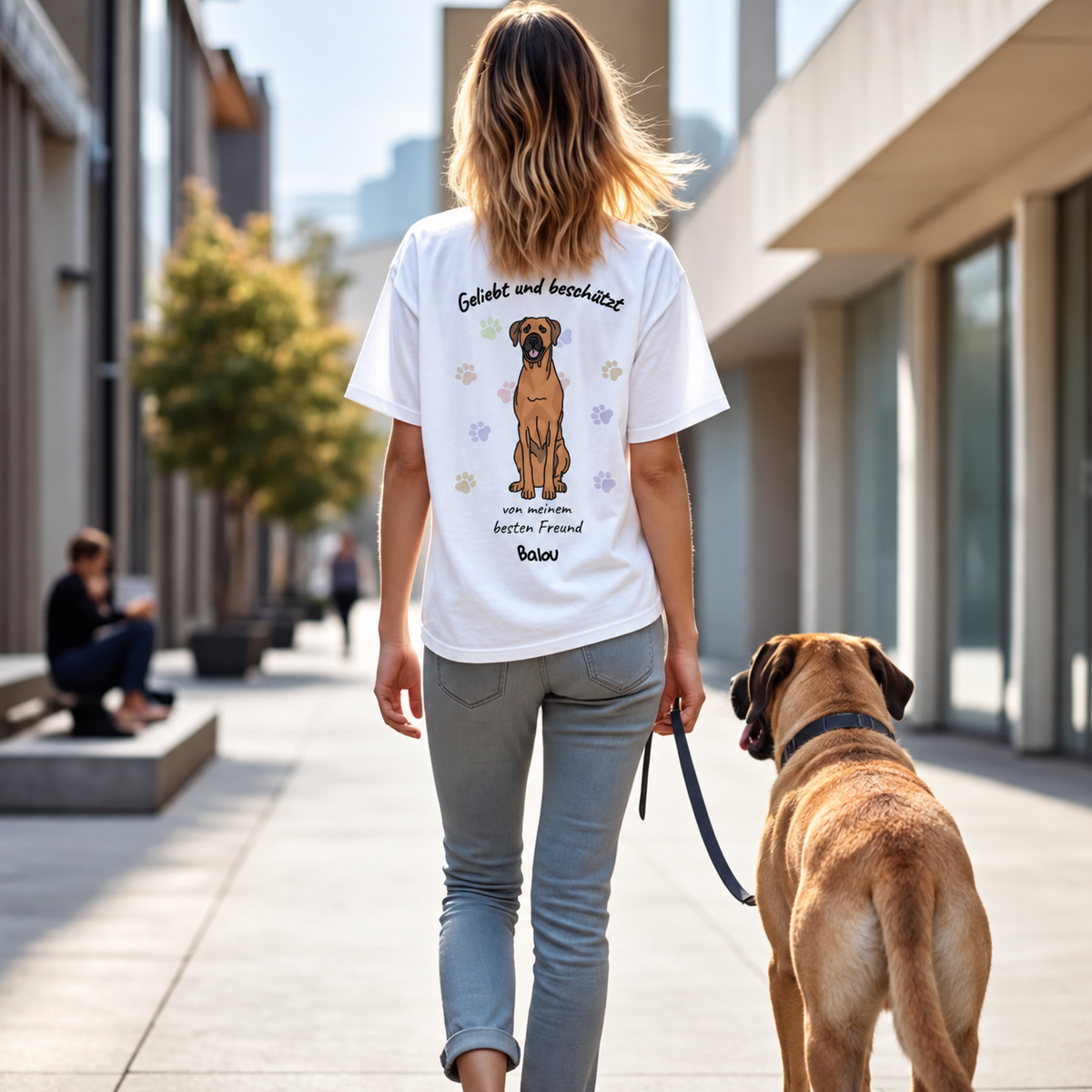 T-shirt bianca con stampa di cane e il testo "Geliebt und beschützt" sul retro, indossata da una donna.