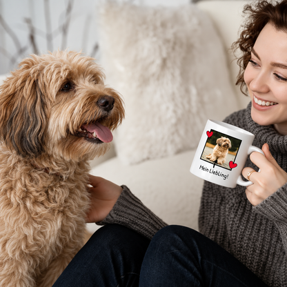 Persona che beve da una tazza bianca con foto di cane e scritta, seduta accanto a un cane.