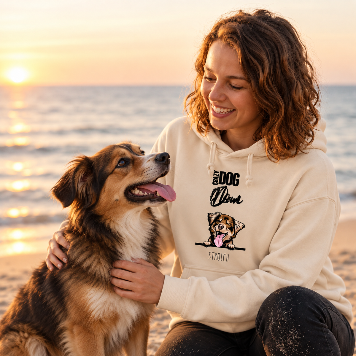 Felpa con cappuccio beige con motivo di cane, indossata da una persona in spiaggia al tramonto.
