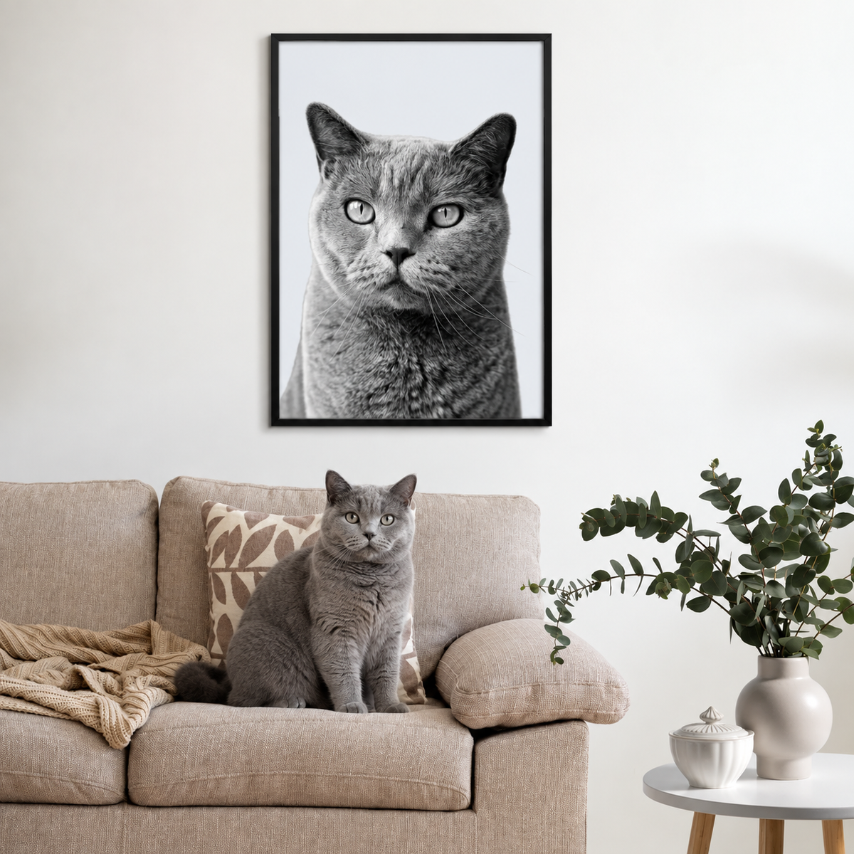 Ritratto grigio di animale incorniciato sopra un divano beige con un gatto grigio simile davanti.