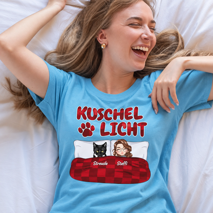 T-shirt blu con la scritta "Kuschel Licht" ed elementi grafici di due persone e un animale nero.