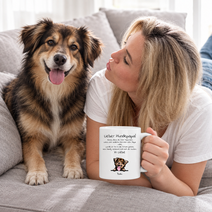 Donna con tazza personalizzata "Lieber Hundepapa" e cane su un divano grigio. Tazza bianca con testo e illustrazione.