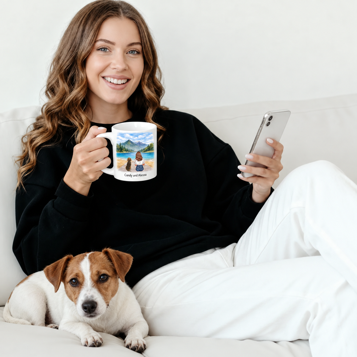 Persona che tiene una tazza personalizzata con paesaggio, un cane sdraiato accanto sul divano.