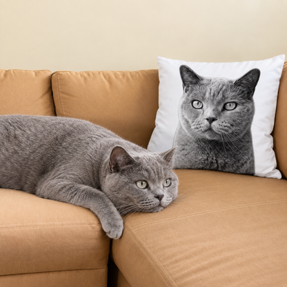 Cuscino grigio e bianco con ritratto di animale su un divano marrone, accanto un gatto grigio.