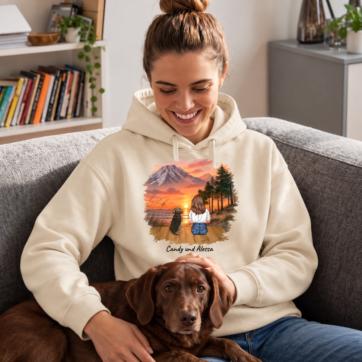 Felpa con cappuccio beige con stampa personalizzata di una donna e un cane al tramonto, seduta su un divano con un cane.