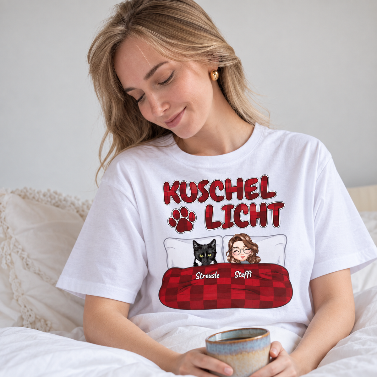 T-shirt bianca con la scritta "Kuschel Licht" e illustrazioni di una donna e un gatto a letto.