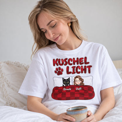 T-shirt bianca con la scritta "Kuschel Licht" e illustrazioni di una donna e un gatto a letto.