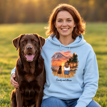 Giacca con cappuccio azzurra con grafica di persona e cane davanti a un paesaggio al tramonto.