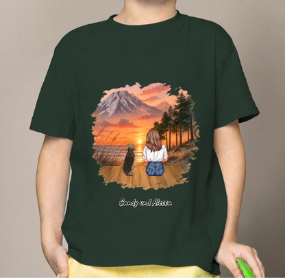 T-shirt per bambini verde scuro con stampa colorata di una ragazza e un cane al tramonto.