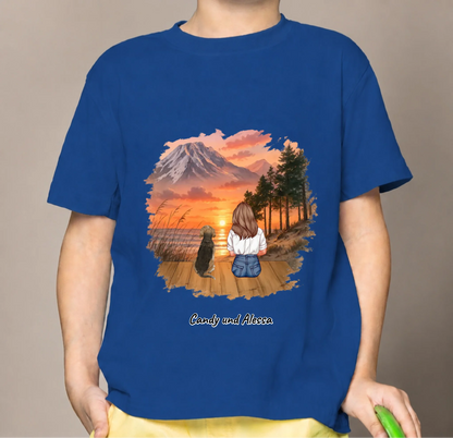 T-shirt per bambini blu con illustrazione di una ragazza e un cane che guardano il tramonto.