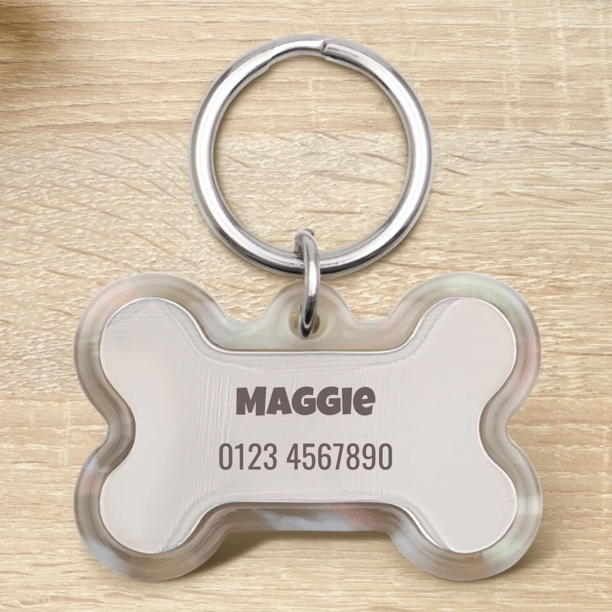 Medaglietta per cane in resina personalizzata a forma di osso con il nome "Maggie" e un numero di telefono.