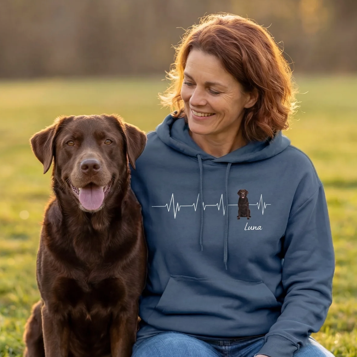Felpa con cappuccio blu personalizzata con motivo battito cardiaco e foto di cane. Donna seduta con il cane sul prato.