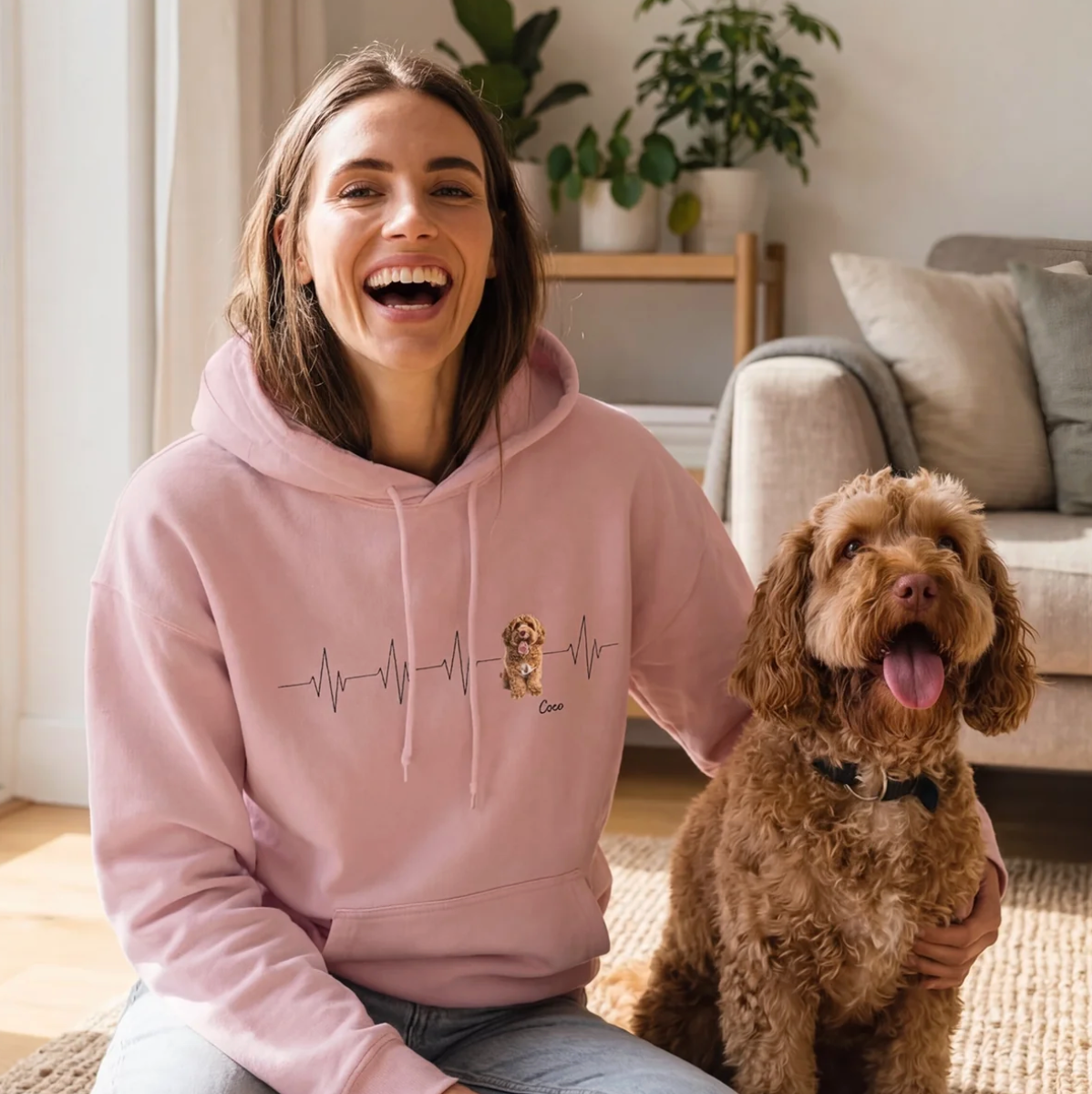 Persona con felpa rosa con motivo battito cardiaco, seduta su un tappeto accanto a un cane.