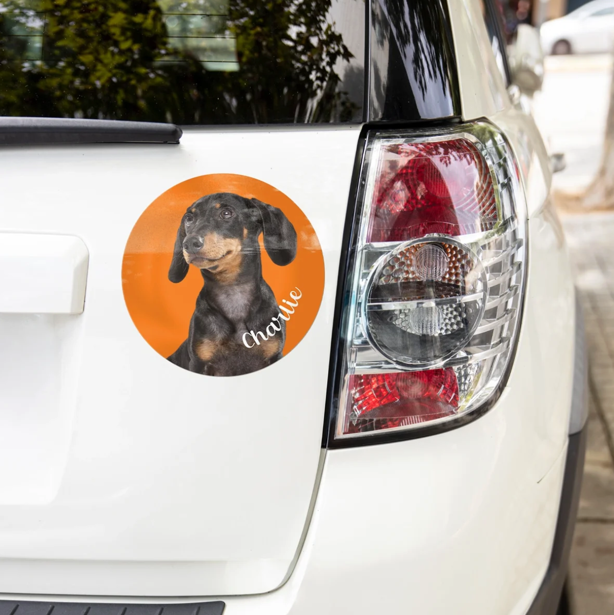 Adesivo per auto personalizzato con immagine di un bassotto su sfondo arancione, applicato su un'auto bianca.
