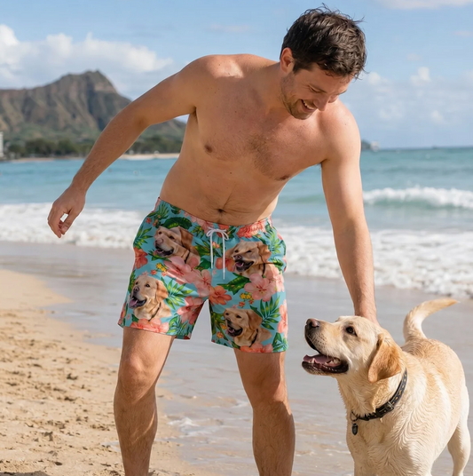 Uomo in spiaggia con costume colorato con cani e fiori. Un labrador gioca nella sabbia accanto a lui.