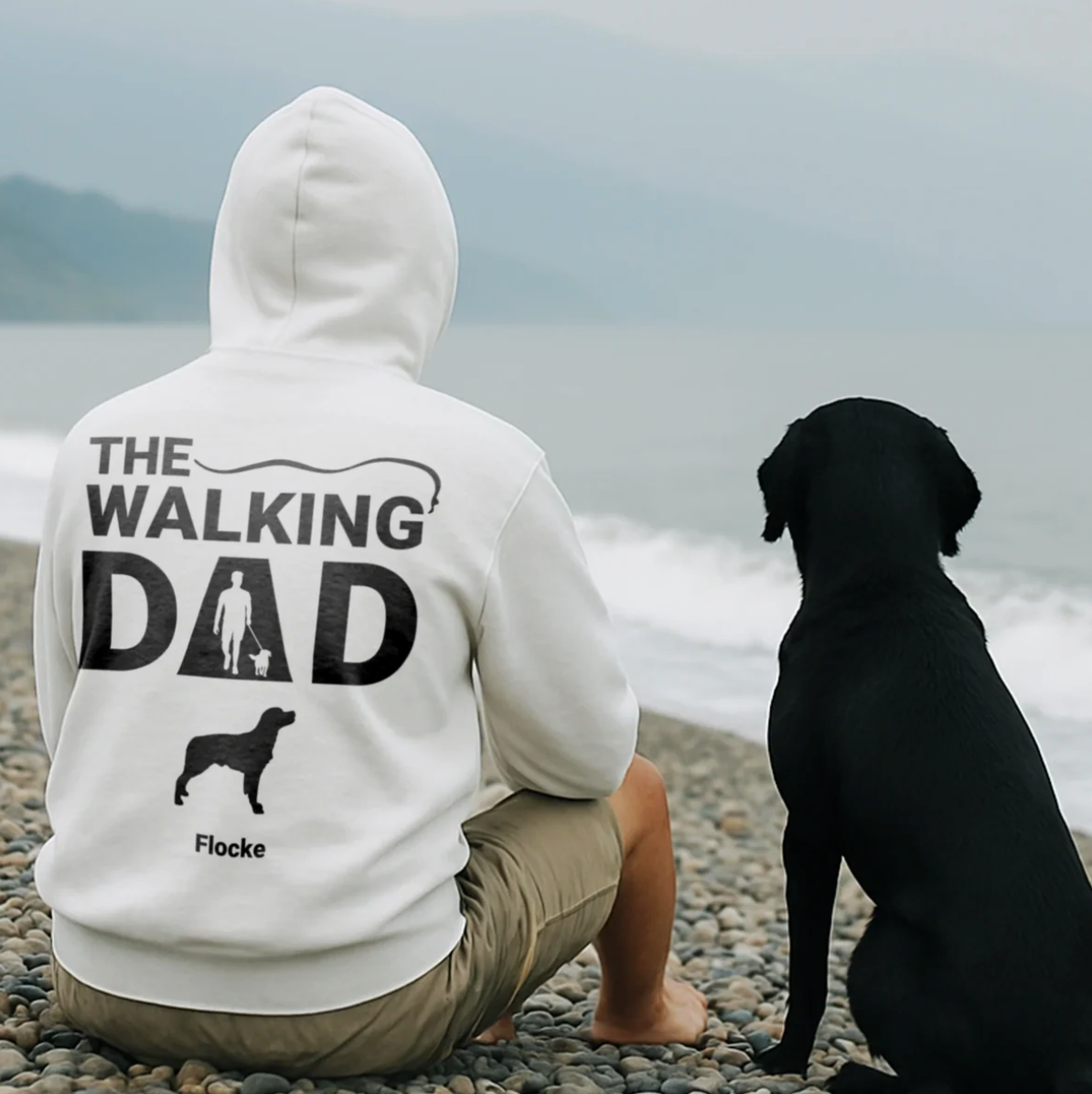 Felpa con cappuccio bianca con stampa sul retro "THE WALKING DAD" e motivo di cane, indossata da un uomo seduto in spiaggia.
