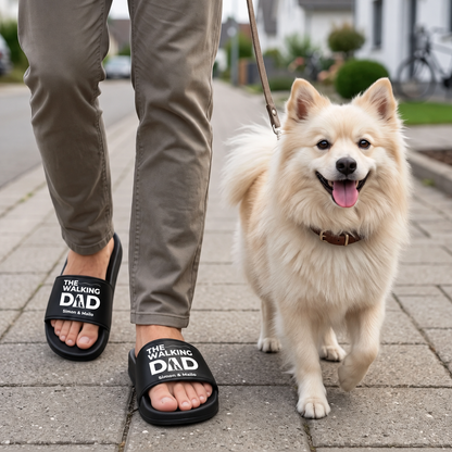 Persona che indossa ciabatte nere personalizzate con la stampa "THE WALKING DAD" mentre porta a spasso un cane.